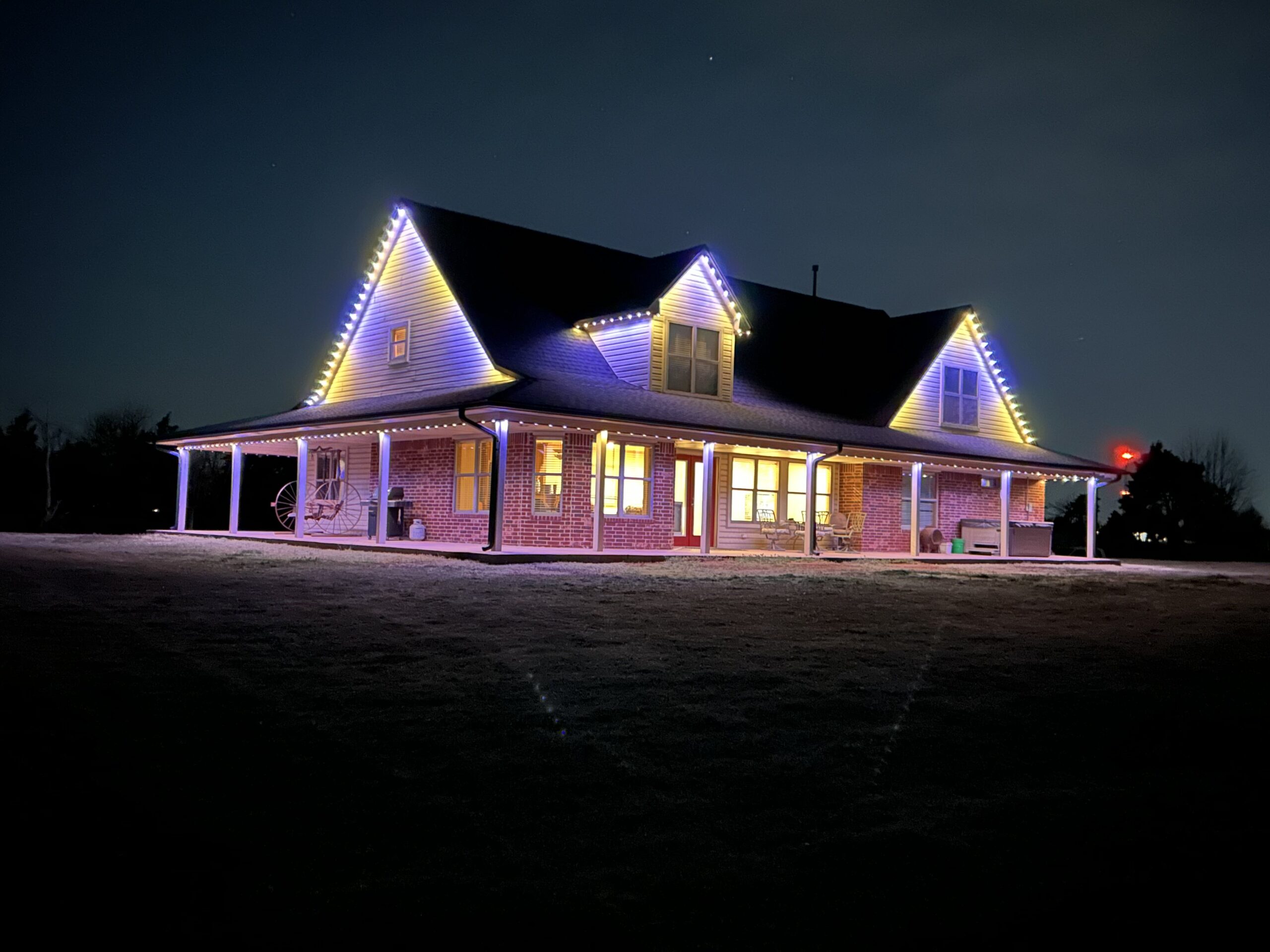Two-story house with permanent holiday lighting displaying festive multi-color LED patterns along the roofline at night